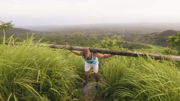 健美运动员训练斜坡与沉重的木条在肩膀在野生自然风景。男子使用木材酒吧举重健身房户外。热带地区运动员训练. — 图库视频影像
