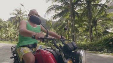 Tropikal manzara yolda motosiklet sürme kıdemli adam. Yeşil palmiye ağaçları arka planda motosiklet üzerinde sürüş güneş gözlüğü yaşlı adam. Motosiklet seyahat konsepti.