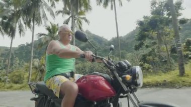 Yakışıklı adam Moped Sürücüsü bisiklet üzerinde yolda tropikal palmiye ağacı arka planda sürme. Yaz tatilinde motosiklet üzerinde seyahat yaşlı adam.