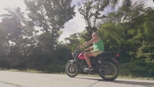 Man motorcyclist driving on motorbike on road with green palm trees landscape. Mature man riding motorcycle on road in tropical palm while summer travel. Moto trip. — Stock Video