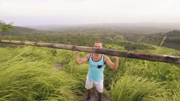 Athlete man lifting heavy wooden bar on tropical hill and highlands landscape. Bodybuilder training press exercise with wooden barbell while outdoor gym in tropics. Lifting weight concept. — Stock Video