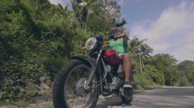 Yeşil orman ve mavi gökyüzü arka planda yolda motosiklet üzerinde Binicilik olgun adam. Düşük açı görünümü. Motosiklet seyahat ederken emekli adam motorsiklet sürüş.