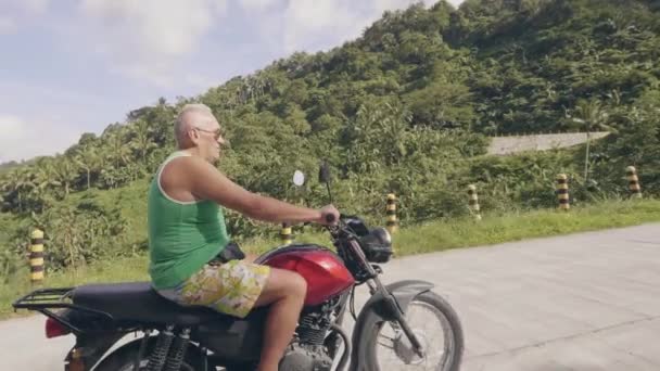 Pria dewasa pengendara sepeda motor bepergian dengan sepeda motor di alam tropis. Senior mengemudi sepeda motor di jalan pedesaan di hutan hujan tropis dan lanskap dataran tinggi . — Stok Video