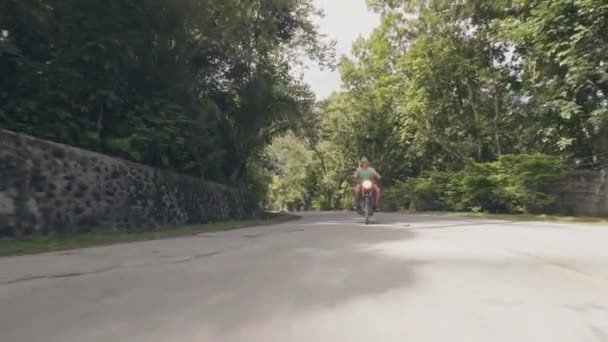 Ενήλικος άνθρωπος μοτοσικλετιστής ιππασία σε μοτοσικλέτα σε προαστιακό δρόμο σε πράσινα δέντρα τοπίο. Ανώτερος άνθρωπος ταξιδεύει με μοτοσικλέτα σε τροπικό δρόμο. — Αρχείο Βίντεο