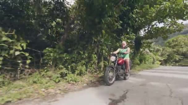 Senior férfi lovaglás motorkerékpár úton a trópusi falusi táj. Érett férfi vezetési motorkerékpár, míg Moto Trip a nyári kirándulás. Motorkerékpár-életmód. — Stock videók