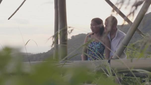 Hombre feliz abrazando a chica joven en verdes colinas paisaje cubierto bosque tropical. Pareja romántica abrazando y disfrutando del paisaje tropical en la fecha de la noche . — Vídeo de stock