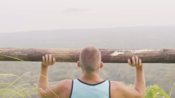 Atlet man lyfta vikt med trä skivstång medan utomhusträning. Fitness man gör press övning med tunga timmer bar på natur bakgrund. Utomhus gym Workout. — Stockvideo