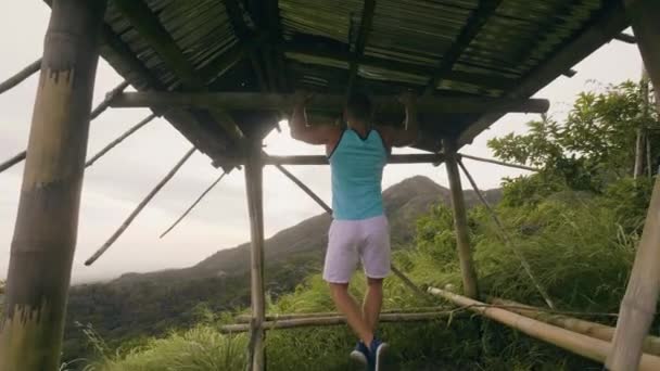 Fitness man entrenamiento tirando de ejercicio en barra horizontal en el bosque tropical. Atleta hombre haciendo pull up entrenamiento en el travesaño al aire libre. Deporte y estilo de vida saludable . — Vídeo de stock