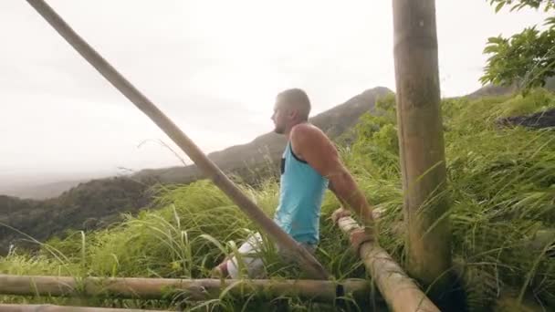 Pohledný muž, který provádí cvičení na zeleném pahorku a tropické Vysočině. Bodybuilder cvičte pro svalstvo ramen na tropickou krajinu. Mužský trénink venku.