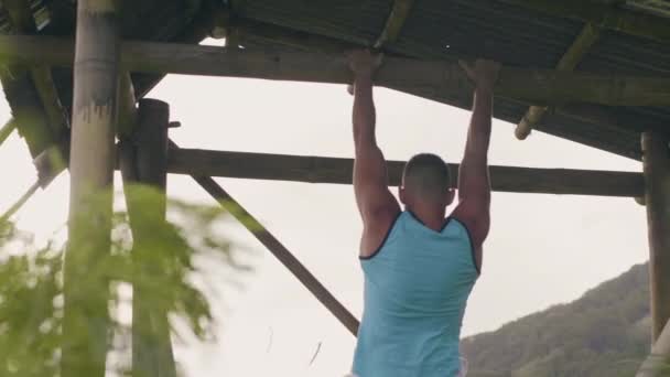 Sportovní muž zavěšený na dřevěném křížovém výcviku ABS je ve venkovním prostoru. Samec se rozpracovní na vodorovném baru. Zpět zobrazit sportovec trénink žaludeční svaly venku. — Stock video