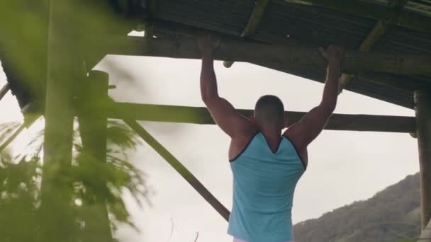 Deporte hombre colgando de madera travesaño entrenamiento abs músculos al aire libre. Ejercicio de abdominales masculinos en barra horizontal. Atrás ver atleta hombre entrenamiento estómago músculos al aire libre . — Vídeo de stock