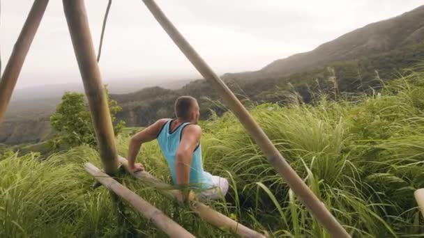 Sportmann beim Liegestütztraining für Trizepstraining an der Holzstange im Freien. Sportler beim Liegestütztraining für das Handtraining vor dem Hintergrund tropischer Natur. Fitnesstraining im Freien. — Stockvideo