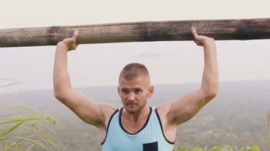 Doğal peyzaj ahşap barbell ile Fit adam eğitim basın egzersiz. Güçlü adam egzersiz açık ağırlık kaldırmak için ağır ahşap bar kullanarak. Spor motivasyonu.