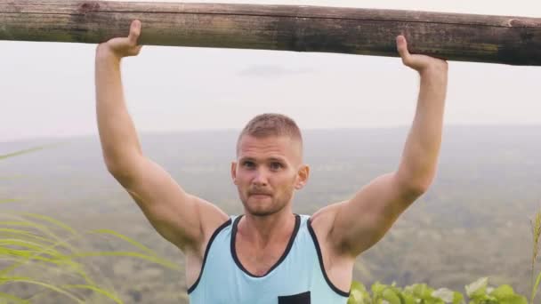 Stark man Training press övning med trä skivstång på tropiska kulle landskap. Bodybuilder man lyfta vikt med timmer bar på utomhus träning. Idrottare man utbildning i tropikerna. — Stockvideo