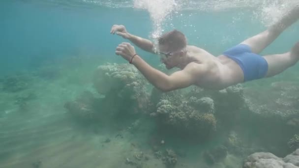 Happy tourist man freediver in a mask is swimming underwater among coral reef in ocean floor. Tropical vacation concept. — Stock Video
