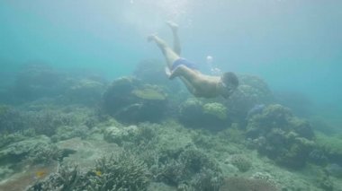 Young man is snorkeling in beautiful ocean and looking at tropical fish and coral reef underwater.
