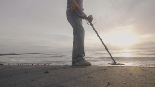 Unrecognizable man with electronic metal detector searches treasures on the ocean tropical sand beach with his dog at sunrise. — Stock Video