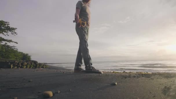 Mann mit Metalldetektor sucht mit Hund bei Sonnenaufgang Schätze am tropischen Sandstrand des Ozeans zwischen den Ruinen. — Stockvideo