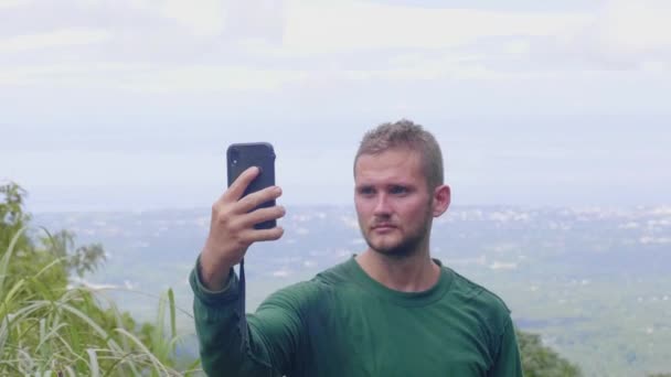 Турист делает селфи по мобильному телефону с панорамным видом с вершины горы. Блогер путешествий позирует для мобильного селфи на ландшафте горной долины с высокой вершины . — стоковое видео