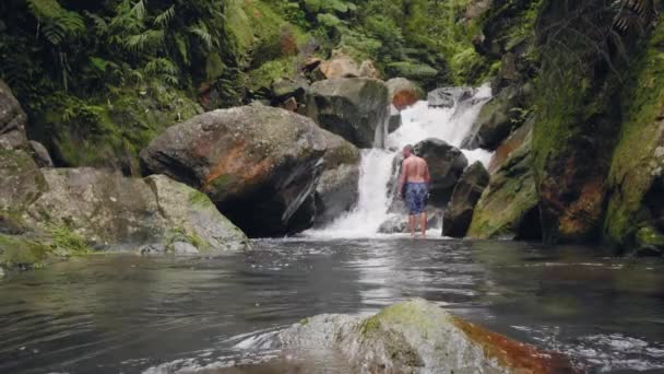 Traveling man på tropiska vattenfall landskap i regnskog. Turist man stående på bakgrund flödande Mountain River i vattenfall i vild djungelskog. — Stockvideo