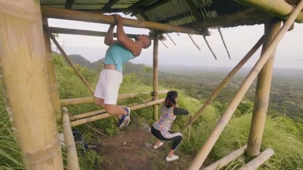 Fitness pareja entrenamiento deporte ejercicio juntos en terreno al aire libre en el paisaje natural. Hombre haciendo ejercicio al aire libre. Fit ejercicio de sentadilla de entrenamiento de mujer en el paisaje tropical . — Vídeo de stock