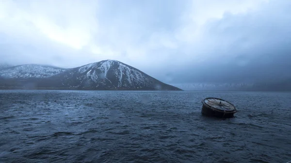 山の背景に帆船を係留するための海水に浮かぶ大きな樽. — ストック写真