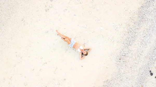 Ung kvinna som ligger på vit sand vid havet utsikt över stranden. Flygfoto från drönartjejen i shorts och bikini liggande på vit sandstrand. — Stockfoto