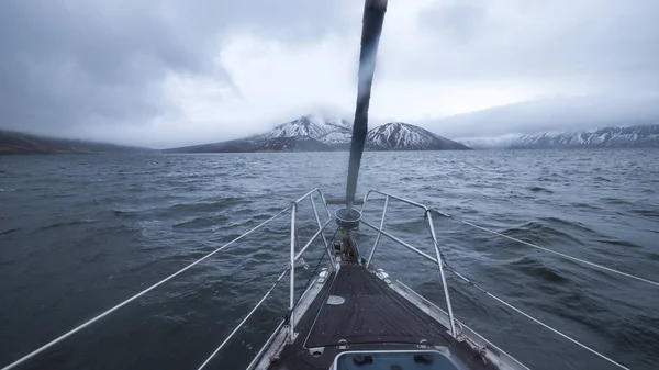 弓帆船在多云的山上与雪峰和蓝色的海景。从海上漂浮帆船的船头到地平线上的雪山的视角. — 图库照片