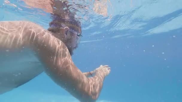 Медленное движение молодой человек в очках плавает под водой открытый бассейн в курортном отеле. Водная линия мужской пловец в открытом бассейне летней гостиницы . — стоковое видео