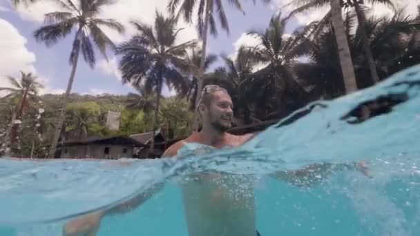 Fröhlicher Mann genießt frisches Wasser im Freibad in Zeitlupe. Wasserlinie Blick glückliche Mann Spaß im Schwimmbad in Resort-Hotel im Sommerurlaub. — Stockvideo