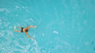 Young man swimming in floating pool aerial view. View from above flying drone male swimmer in swimming pool. Water sport. Summer activity.