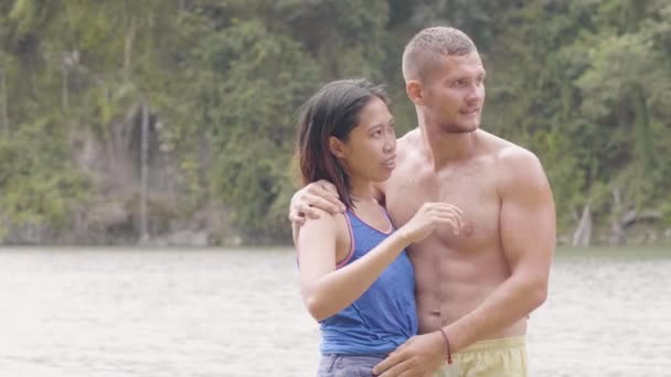Młody mężczyzna i kobieta obejmujący i całujący się na tle tropikalnego wodospadu. mieszane wyścig para Azji kobieta i biały mężczyzna korzystających natura podczas lato wakacje. — Wideo stockowe