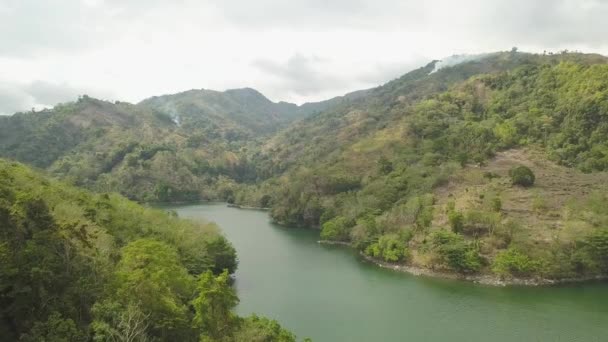 Tropické jezero a zelená vrchoviny jsou v krajině od létající vody. Vzdušné krajiny zelené kopce pokryté tropickými rostlinami a řekou na oblačném pozadí. — Stock video