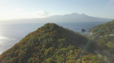 Ufukta dağ silueti ve deniz manzarası üzerinde yeşil tepe. Mavi deniz ve dağ manzara üzerinde uçan drone yeşil yayla yukarıdan görünümü.