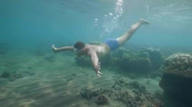 Maskeli sportif adam dalış yapar ve mercanlar üzerinde tatilde okyanusta su altında yüzer.