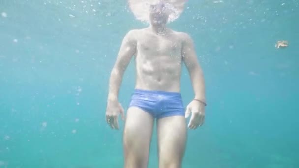 Happy young man underwater waves hands smiles and looks at camera on vacation. — Stock Video