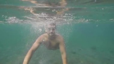 Maskeli adam su altında dalış ve okyanusta tropikal tatil kameraya bakar.