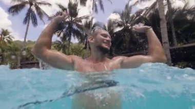 Gülen sakallı adam yüzme havuzunda atlıyor ve su sıçratıyor, yavaş çekimde su altından vuruldu.