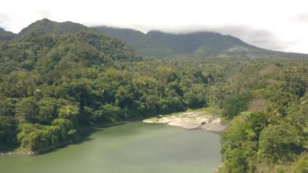 Vzdušné Panorama tropického lesa na břehu jezera a zelených horách na oblačné obloze. Drone pohled na zelené hory pokryté deštním lesem na pobřeží tropického jezera. — Stock video