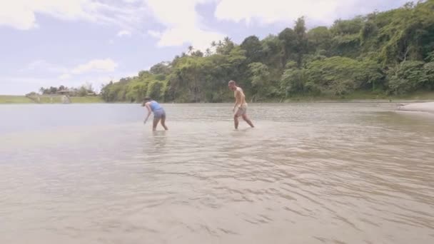 Loving couple man and woman are splashing water on the lake in tropical island. — Stock Video