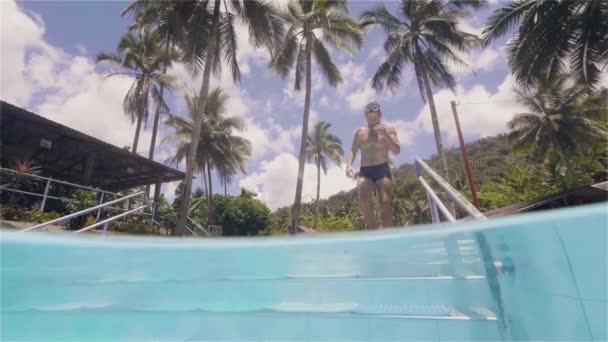 Genç adam tropik adada lüks otelde dinleniyor havuz merdivenlerinde aşağı inerek yüzmek için gidiyor. — Stok video