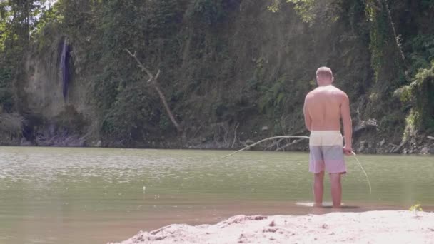 Молодой человек рыбачит на озере среди гор . — стоковое видео