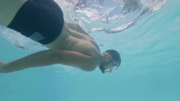 Podwodny widok młodego mężczyznę w goglach pływackich w niebieskim basenie wodnym. Brodaty pływak pływający w basenie zwolnionym tempie. — Wideo stockowe