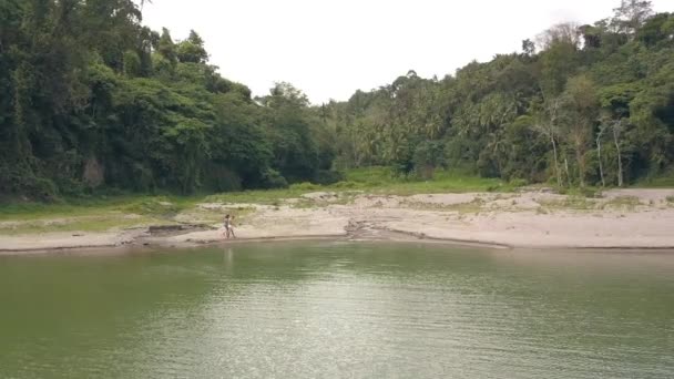 Junges verliebtes Paar beim Spazierengehen am Seeufer auf tropischen Regenwald-Landschaft Luftaufnahme. Touristenpaar wandert am tropischen Flussufer auf grünem Dschungel-Waldhintergrund. — Stockvideo