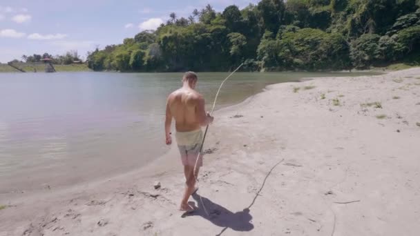 Pescatore con asta fatta a mano sta camminando sulla spiaggia di sabbia per la pesca sul lago . — Video Stock