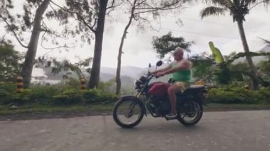 Asya kırsalında dağ yolunda motosiklet kullanan olgun adam. Yeşil tepeler ve yağmur ormanları manzara moto gezi sırasında motosiklet üzerinde seyahat Turist adam.