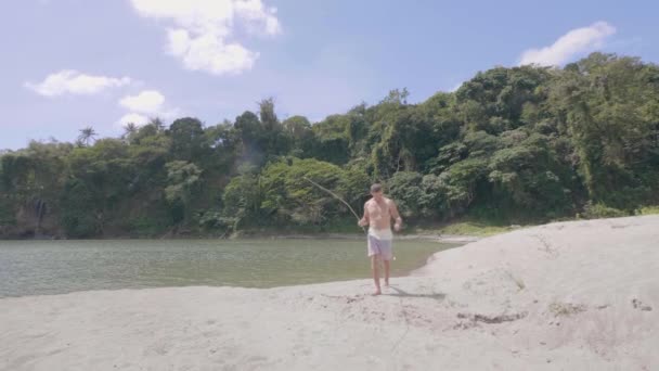 Jonge man loopt op zandstrand op het meer met handgemaakte hengel. — Stockvideo