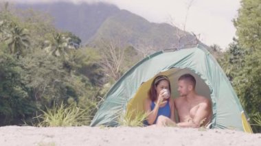 Genç çift doğada dinleniyor. Çadırda çay içip gülüyorlar..