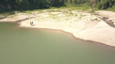 Çift erkek ve kadın tropikal orman, havadan görünümü arasında göl üzerinde kum plajda yürüyorlar.