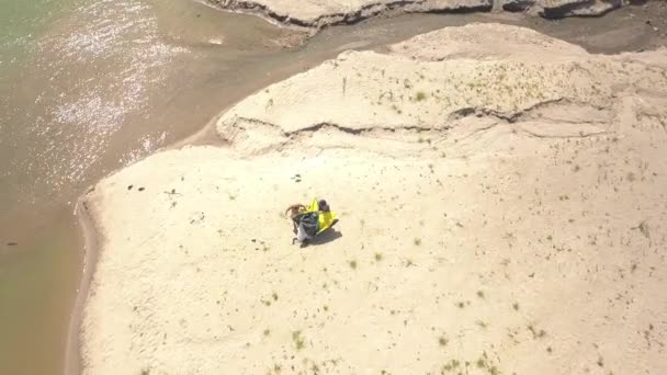 Couple dismantle a tent on the lake sand beach, aerial view. — Stock Video